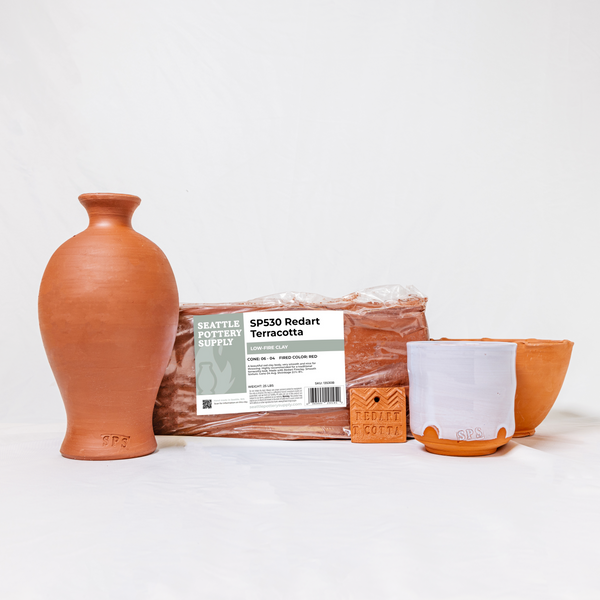 A grouping of a vase, block of wet clay, test tile, bowl, and cup made from Happycozygoods Redart Terracotta clay. The clay block includes a Happycozygoods brand label.