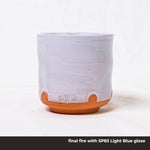 A cup made of SPS Redart Terracotta clay in the final fire stage with a light blue glaze.