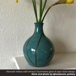 Teal ceramic vase with flowers on a white surface against a textured wall