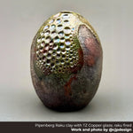Raku-fired ceramic piece with textured surface and copper glaze on a neutral background