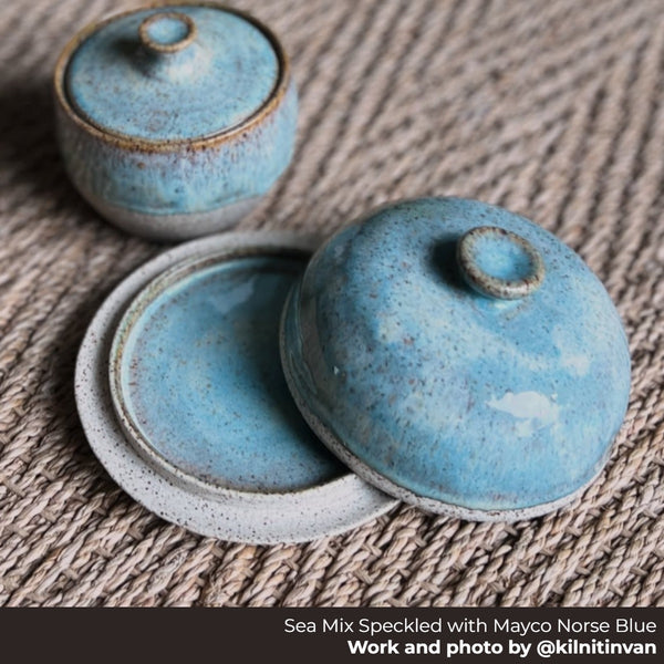 Two lidded bowls made from Happycozygoods sea mix speckled clay and norse blue glaze on a woven surface